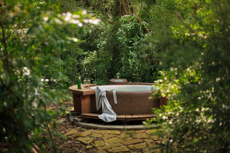 A wooden hot tub in a garden, with a folded cover resting on the rim