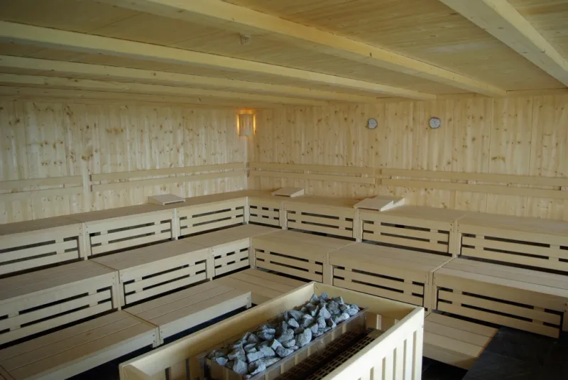 Inside a wood-lined sauna with tiered benches and a stone-topped heater in the corner